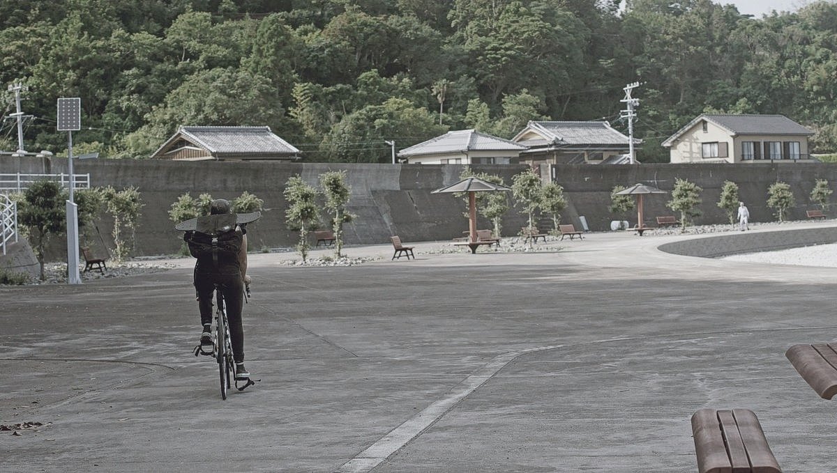 rek riding their bike in minamiise, japan, with a pennyboard strapped to their backpack