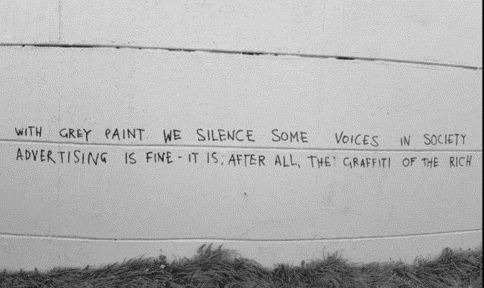 text written on a wall once covered with graffiti that was recently painted over: with grey paint we silence some voices in society. Advertising is fine- it is, after all, the graffiti of the rich.